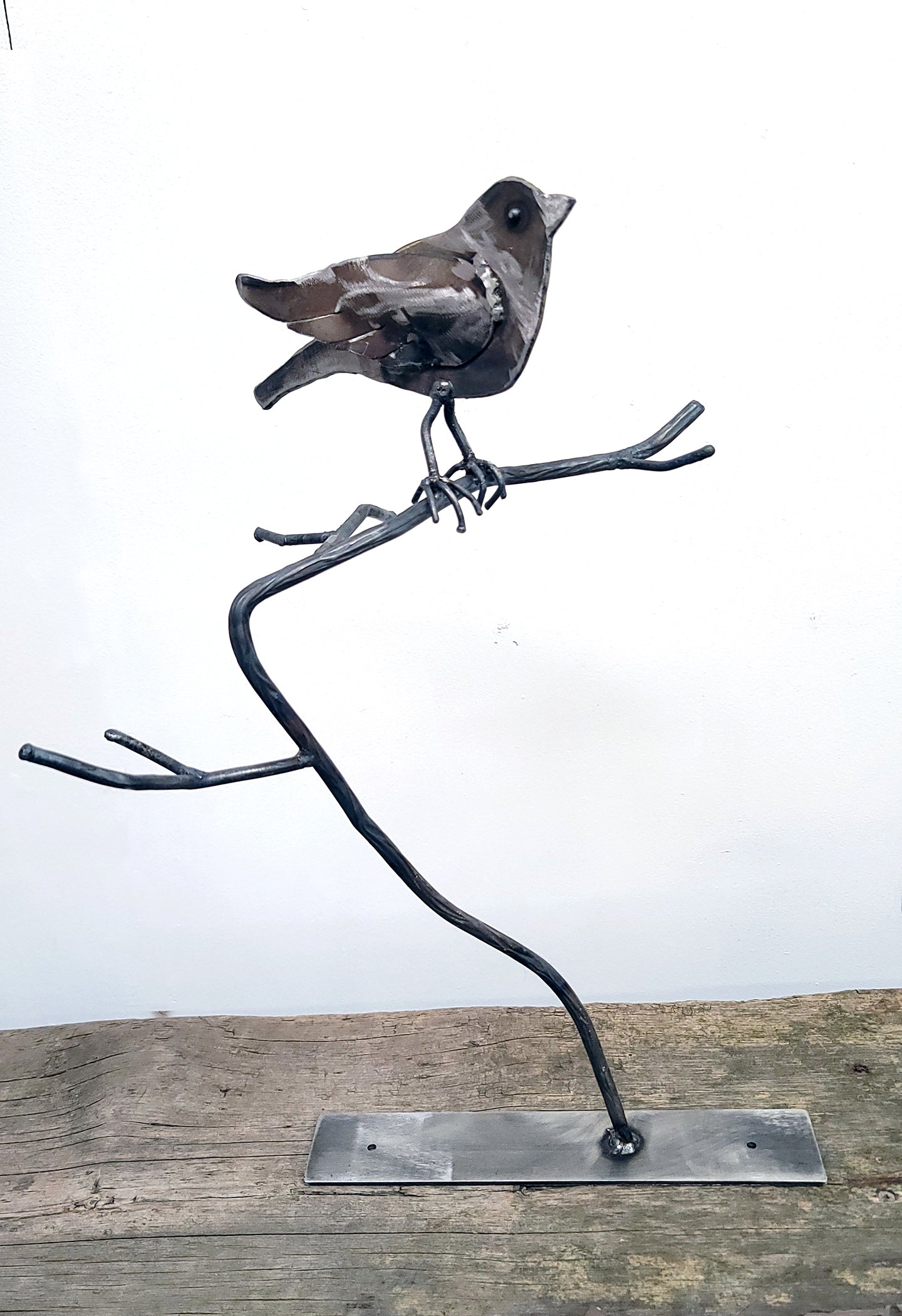 metal bird sits on a branch on a small steel rectangle base